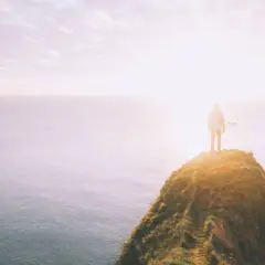 Ein Mensch steht auf einer Klippe am Meer, die Sonne blendet. Was tun bei einer Lebenskrise? Der Blick in die Weite gibt Hoffnung.
