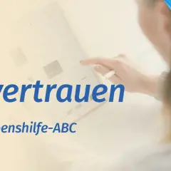 Ein Tablet zeigt Grafiken, während eine Hand mit einem Stift darauf tippt. Der Text "Urvertrauen aufbauen" und "Das Lebenshilfe-ABC" ist zu sehen.