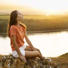 Junge Frau genießt den Sonnenuntergang auf einem Felsen, ein Bild für ein sorgenfreies Leben.