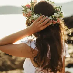 Frau mit Blumenkranz am Kopf, genießt die Sonne am Meer. Ein Bild von Mittsommer Ritualen.