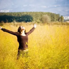 Frau mit ausgebreiteten Armen in einem goldenen Feld, die den Himmel umarmt. Ein Gefühl von Freiheit und der 7. Sinn spirituell.