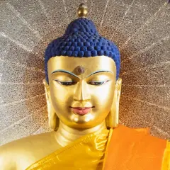 Goldene Buddha-Statue mit blauem Haar und orangefarbenem Gewand vor einem schimmernden Heiligenschein. Ein Wegweiser, wie werde ich buddhist.