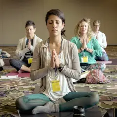 Frauen in einer Gruppe praktizieren transzentale Meditation, sitzen im Schneidersitz mit gefalteten Händen und geschlossenen Augen.