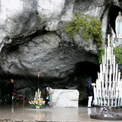 Pilger beten in der Lourdes Grotte Bernadette. Eine Marienstatue und Kerzen stehen in der Höhle.