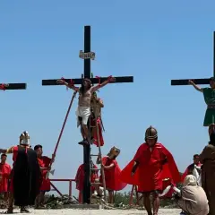 Nachstellung, wie Jesus stirbt am Kreuz, mit zwei weiteren Männern, die ebenfalls gekreuzigt werden. Soldaten in römischer Kleidung und Zuschauer sind anwesend.