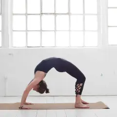 Frau in schwarzer Kleidung in einer Brückenpose, eine der yoga posen schwer, die Kraft und Flexibilität zeigt.