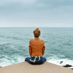 Frau sitzt am Meer, blickt in die Ferne und denkt über wichtige entscheidungen im leben nach.