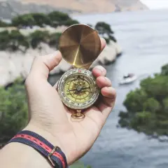 Eine Hand hält einen Kompass über einer Bucht. Die Frage, was mit dem Leben anfangen, wird durch die Suche nach Richtung symbolisiert.
