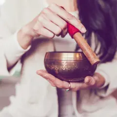 Hände halten eine Klangschale, bereit, sie mit einem Holzklöppel anzuschlagen. Die **Klangschalen Wirkung** entfaltet sich in sanften Tönen.