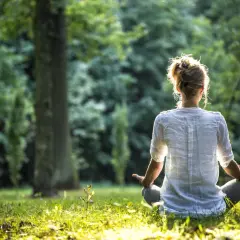 Frau in weißem Hemd meditiert im Wald. Sie nutzt eine Meditation Mantra Liste zur inneren Ruhe.
