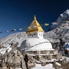 Ein buddhistischer Stupa mit Augen im Schnee, umgeben von Gebetsfahnen, die buddhistische Mantras in den Wind tragen. Majestätische Berge im Hintergrund.