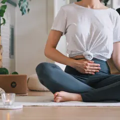 Frau in Lotussitz übt Kapalabhati Pranayama, Hände auf dem Bauch, um die Bauchatmung zu spüren.