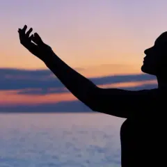 Silhouette einer Frau mit erhobenen Armen vor einem farbenfrohen Himmel und Meer. Sie scheint einen **chant deutsch** zu singen.