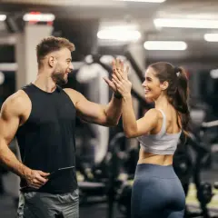 Mann und Frau geben sich im Fitnessstudio einen High Five. Er hält ein Tablet, vielleicht für seine persönliche Coach Ausbildung.