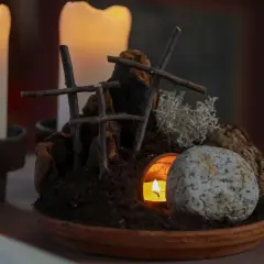 Grab und Kerzenlicht symbolisieren die **heilige Woche**. Ein Stein liegt vor dem Eingang einer Höhle, aus der ein Licht scheint.