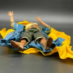 Eine Krippenfigur des heiligen Josef liegt erschöpft auf einem blauen und gelben Tuch.