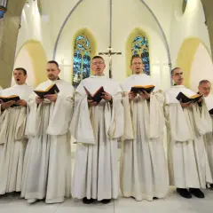 Mönche in weißen Roben singen gregorianik musik aus Büchern in einer Kirche.