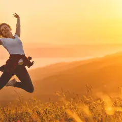 Eine Frau springt voller Freude in der goldenen Abendsonne. Sie ist voller Energie und genießt den Moment in der Natur.
