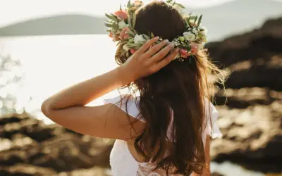 Frau mit Blumenkranz am Kopf, genießt die Sonne am Meer. Ein Bild von Mittsommer Ritualen.