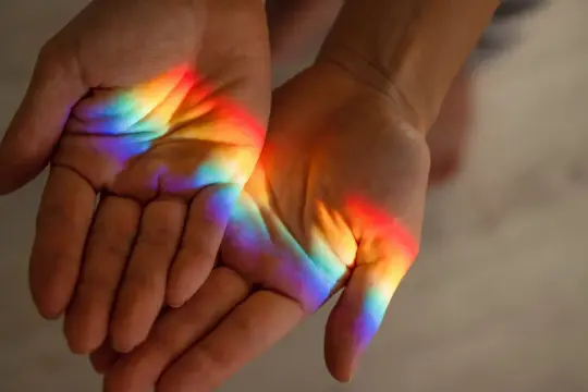 Hände fangen das Licht eines Regenbogens ein, wie ein Symbol der Hoffnung und des Friedens, das an hl. Franziskus erinnert.