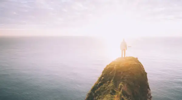Ein Mensch steht auf einer Klippe am Meer, die Sonne blendet. Was tun bei einer Lebenskrise? Der Blick in die Weite gibt Hoffnung.