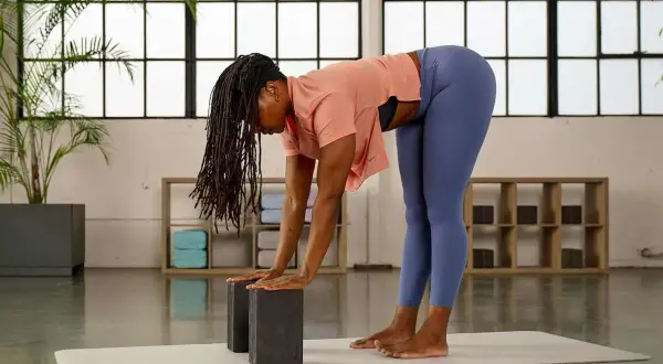 Frau mit Dreadlocks praktiziert Yoga mit Block. Sie beugt sich vor, Hände auf zwei Blöcken, um die Dehnung zu vertiefen.