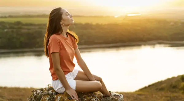 Junge Frau genießt den Sonnenuntergang auf einem Felsen, ein Bild für ein sorgenfreies Leben.