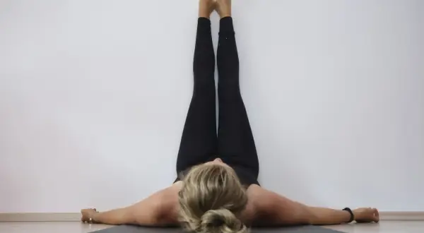 Frau in schwarzer Kleidung praktiziert Yoga Sommer, Beine an der Wand, entspannt auf der Matte liegend.