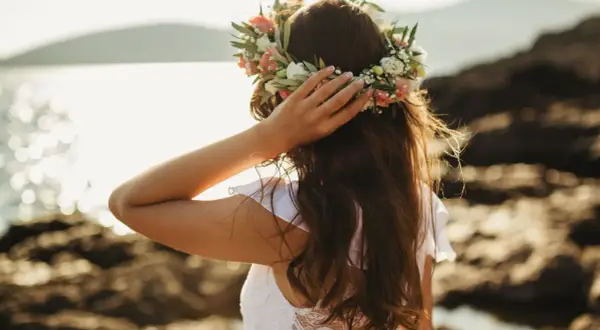 Frau mit Blumenkranz am Kopf, genießt die Sonne am Meer. Ein Bild von Mittsommer Ritualen.