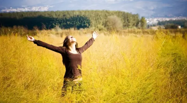 Frau mit ausgebreiteten Armen in einem goldenen Feld, die den Himmel umarmt. Ein Gefühl von Freiheit und der 7. Sinn spirituell.