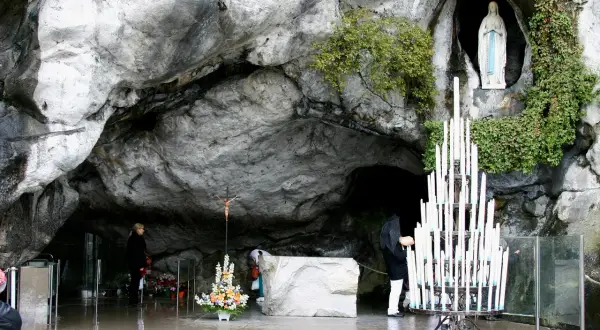Pilger beten in der Lourdes Grotte Bernadette. Eine Marienstatue und Kerzen stehen in der Höhle.