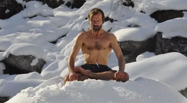 Mann in Lotussitz im Schnee, praktiziert die Wim Hof Methode.