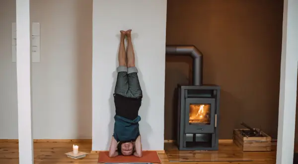 Person in einer Kopfstand-Pose, eine der vielen Iyengar Yoga Asanas, übt vor einem Kaminfeuer.
