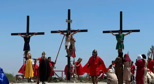 Nachstellung, wie Jesus stirbt am Kreuz, mit zwei weiteren Männern, die ebenfalls gekreuzigt werden. Soldaten in römischer Kleidung und Zuschauer sind anwesend.