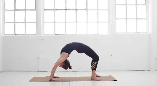 Frau in schwarzer Kleidung in einer Brückenpose, eine der yoga posen schwer, die Kraft und Flexibilität zeigt.