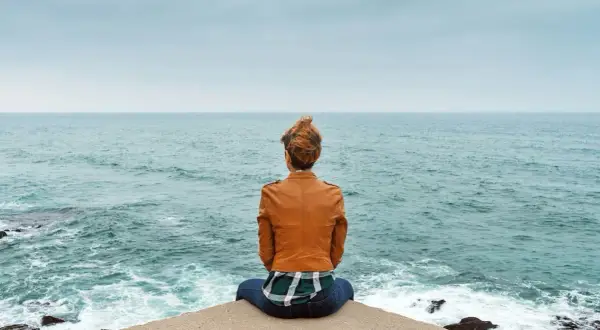 Frau sitzt am Meer, blickt in die Ferne und denkt über wichtige entscheidungen im leben nach.