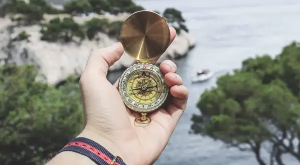 Eine Hand hält einen Kompass über einer Bucht. Die Frage, was mit dem Leben anfangen, wird durch die Suche nach Richtung symbolisiert.