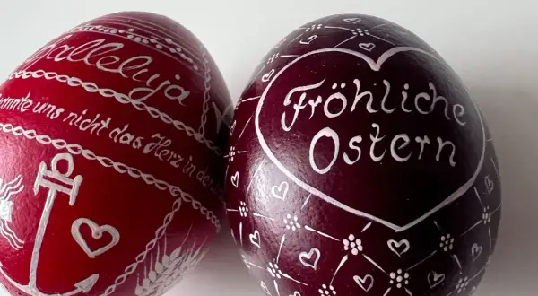 Zwei bemalte Ostereier: Ein rotes mit "Halleluja" und Anker, ein dunkles mit "Fröhliche Ostern" und Herzen. Ein schöner risus paschalis.