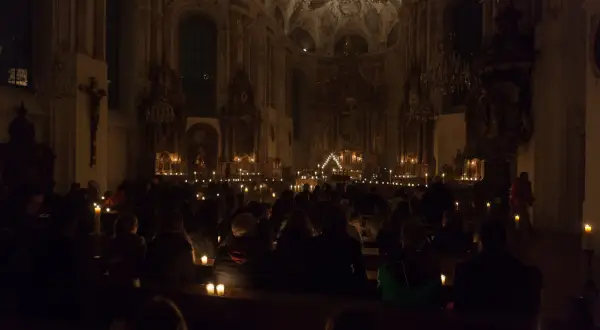 Menschen sitzen in einer dunklen Kirche, beleuchtet von Kerzen. Eine feierliche Vigil in der Kirche.