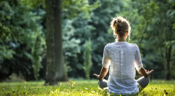 Frau in weißem Hemd meditiert im Wald. Sie nutzt eine Meditation Mantra Liste zur inneren Ruhe.