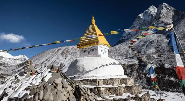 Ein buddhistischer Stupa mit Augen im Schnee, umgeben von Gebetsfahnen, die buddhistische Mantras in den Wind tragen. Majestätische Berge im Hintergrund.