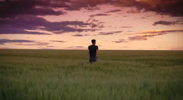 Ein Mann steht in einem weiten Feld, blickt in den dramatischen Himmel. Ein Moment der stillen, **contemplative deutsch** Reflexion.