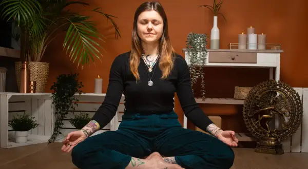 Frau in tiefer meta meditation, umgeben von Pflanzen und Kerzen. Eine Shiva-Statue im Hintergrund.
