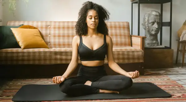 Frau in schwarzer Sportkleidung praktiziert Krafttier Meditation auf einer Matte. Sie sitzt im Lotussitz, Augen geschlossen, Hände im Mudra.