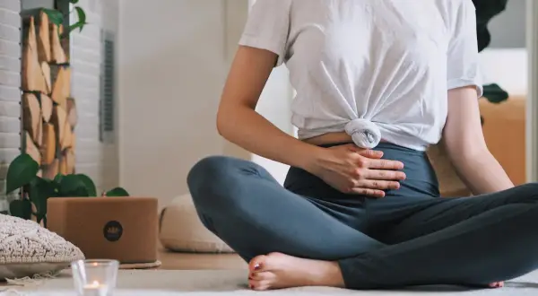 Frau in Lotussitz übt Kapalabhati Pranayama, Hände auf dem Bauch, um die Bauchatmung zu spüren.
