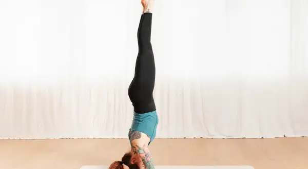 Frau in Kopfstand-Yoga-Pose auf Matte. Die Wirkung dieser Haltung ist belebend und kräftigend.