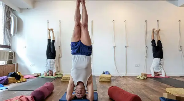 Drei Männer praktizieren im Iyengar Yoga Studio den Kopfstand. Die Iyengar Yoga Wirkung ist spürbar: Kraft, Balance und Ruhe.