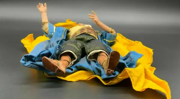 Eine Krippenfigur des heiligen Josef liegt erschöpft auf einem blauen und gelben Tuch.