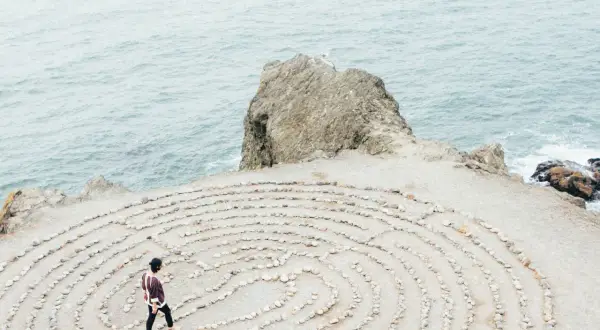Person geht durch einen Steinlabyrinth am Meer. Ein Symbol für die Ausbildung zum spirituellen Coach, die Suche nach innerer Klarheit.