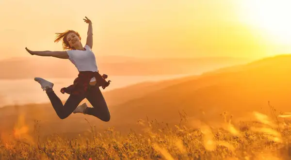 Eine Frau springt voller Freude in der goldenen Abendsonne. Sie ist voller Energie und genießt den Moment in der Natur.